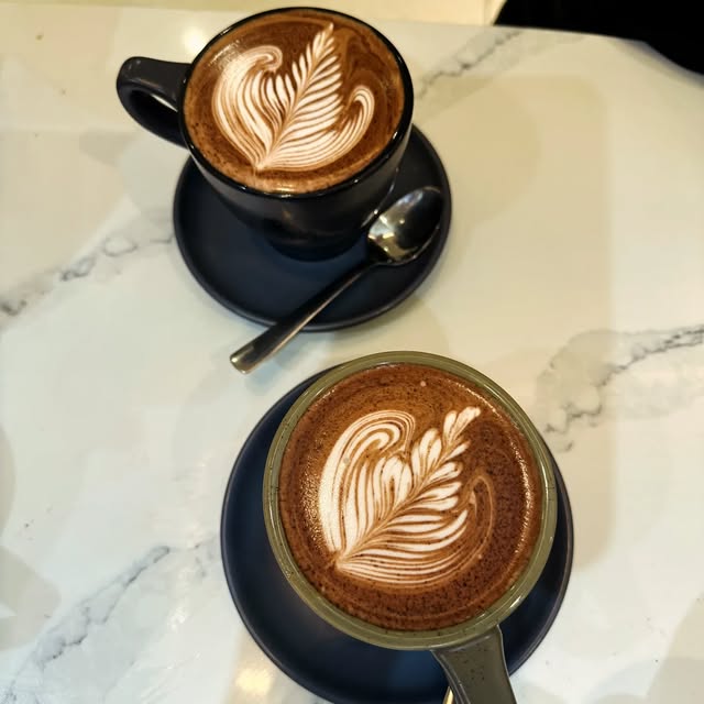Two mochas with rosetta latte art on a marble counter
